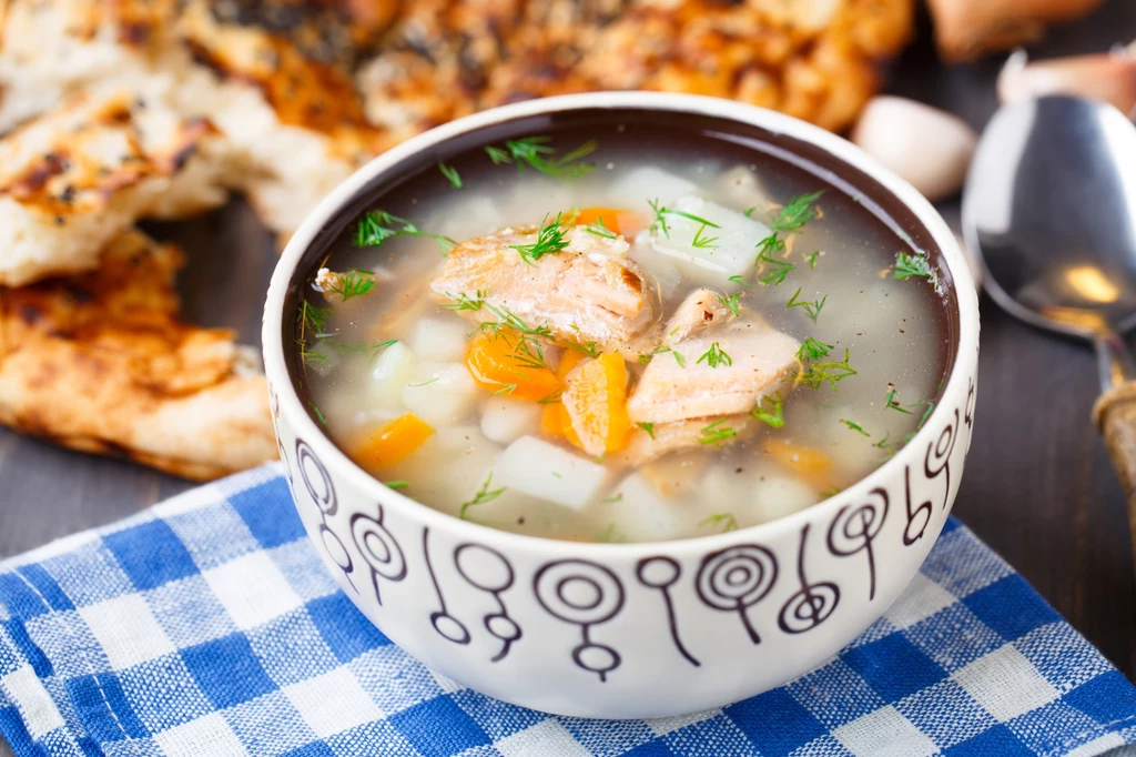 Karaś nadaje się do przyrządzenia zupy rybnej Aromatyczna zupa rybna z kawałkami warzyw i koperkiem podana w dekoracyjnej misce, w tle chleb i widelczyk na serwetce w niebieską kratę.