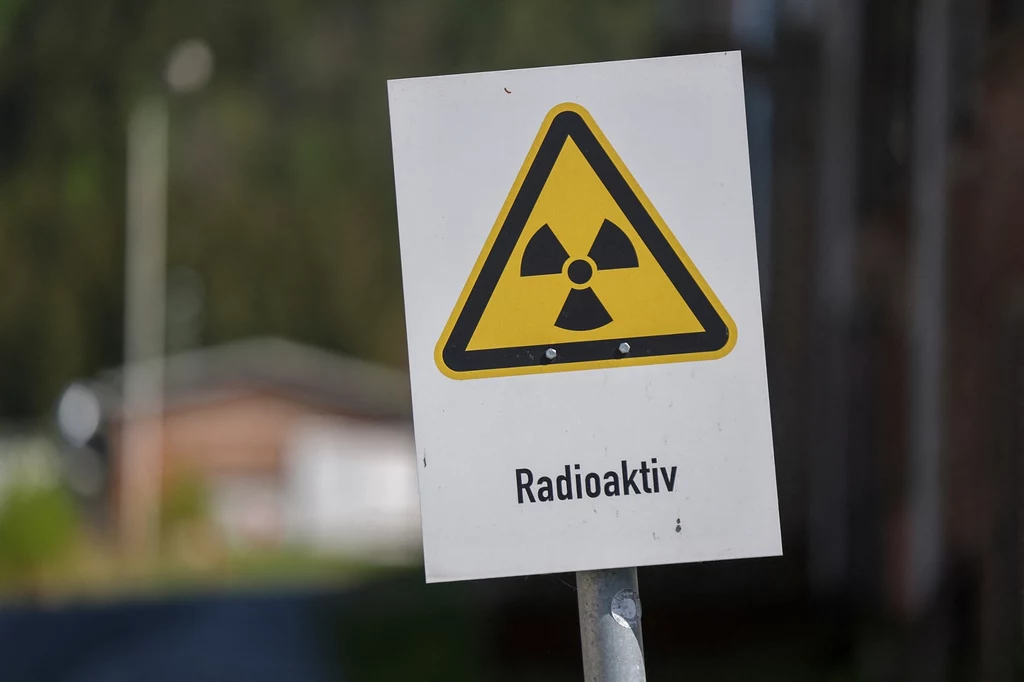 Ruda uranu po obróbce przemienia się w tzw. yellowcake, czyli oczyszczone tlenki uranu, W nich 0.7 proc. składu stanowi izotop U-235. Aby użyć uranu w celach wojskowych izotop U-235 musi obejmować od 90 proc. składu wzwyż Tablica ostrzegawcza z symbolem promieniowania jonizującego oraz napisem 'Radioaktiv', umieszczona na tle rozmytego budynku.