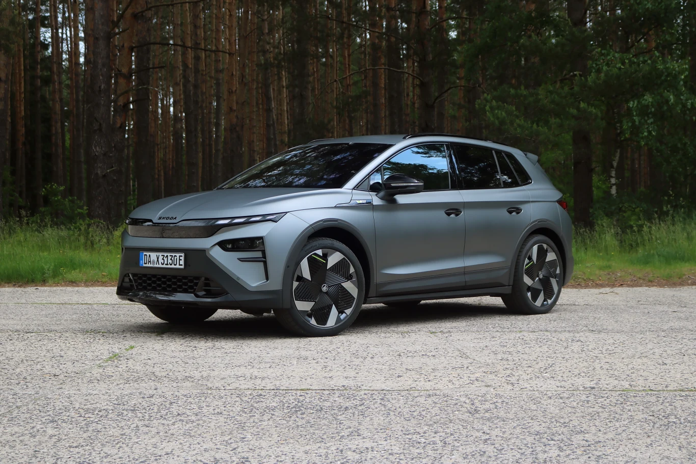 Skoda Elroq RS wjeżdża do Polski. Jest szybka, mocna i wygodna Szary, nowoczesny samochód elektryczny SUV stoi na asfaltowej drodze, w tle znajduje się las sosnowy, auto ma charakterystyczne felgi oraz przyciemnione szyby.