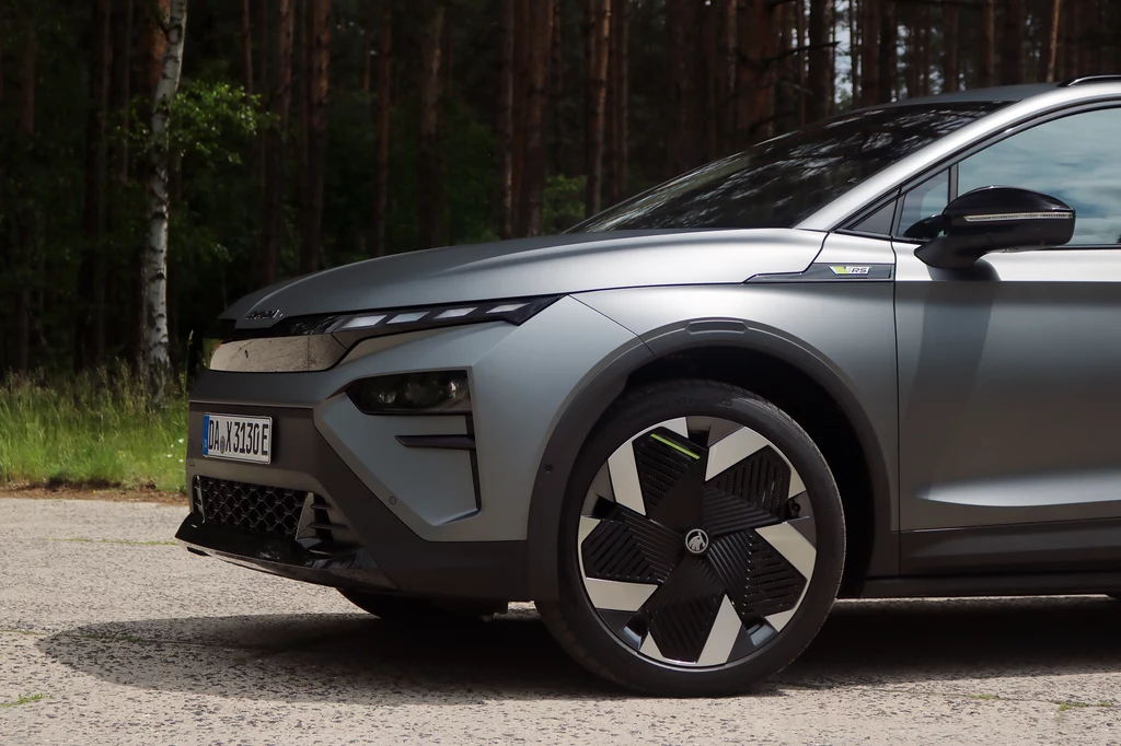 Elroq RS już w standardzie oferuje adaptacyjne zawieszenie DCC. Nowoczesny samochód elektryczny w matowym szarym kolorze, widoczne przednie reflektory, wyraźny wzór na feldze koła oraz fragment tablicy rejestracyjnej, tło stanowi las.