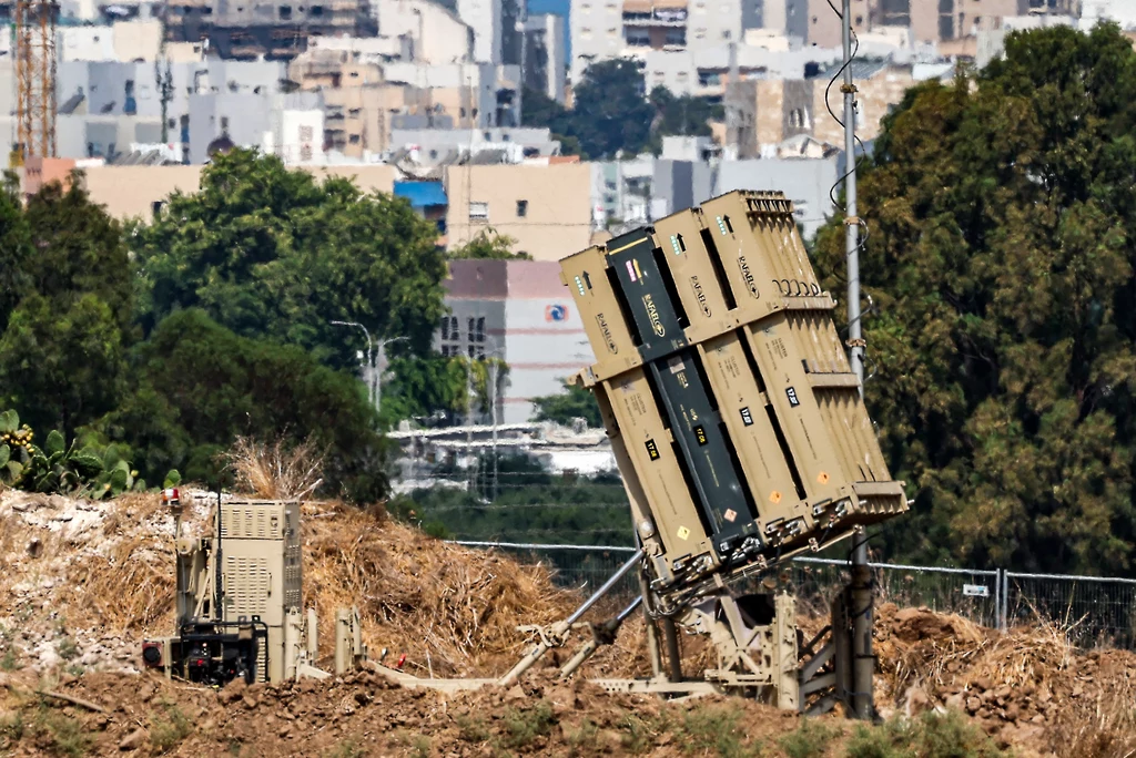 Bateria systemu przeciwlotniczego Iron Dome ustawiona na wzgórzu, w tle widać miejską zabudowę, drzewa oraz elementy infrastruktury.