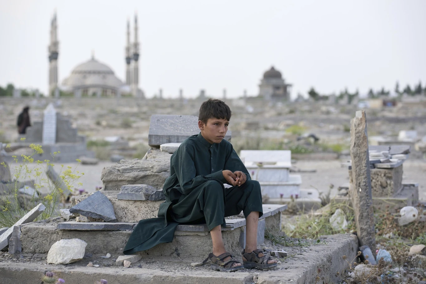 Kabul mierzy się z tragicznym kryzysem wodnym Chłopiec w ciemnym ubraniu siedzi na grobie na cmentarzu, otoczony licznymi nagrobkami, w tle widoczny meczet z dwiema minaretami, krajobraz wywołuje melancholijny nastrój.