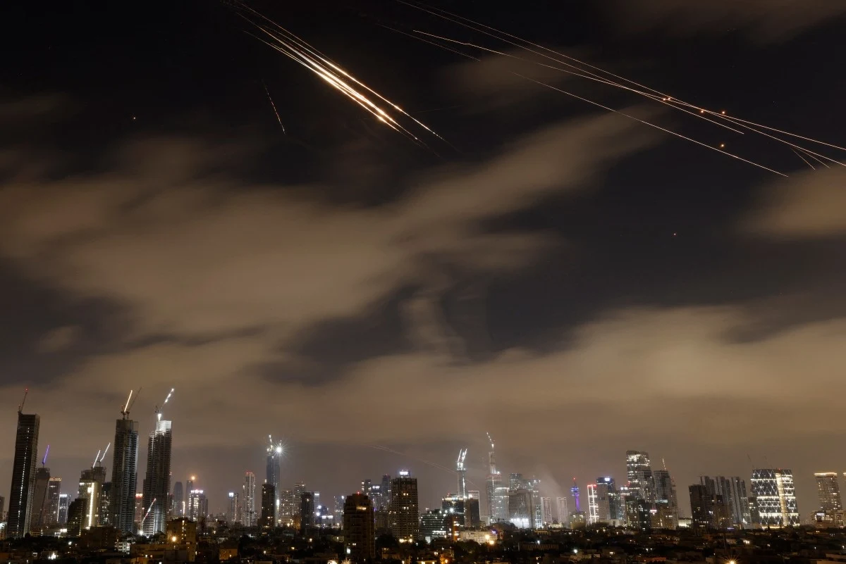 W nocy z soboty na niedzielę po raz kolejny doszło do wymiany ognia między Iranem i Izraelem Rakiety rozświetlają nocne niebo nad nowoczesną panoramą miasta, budynki podświetlone są miejskim oświetleniem, a smugowe ślady rakiet podkreślają intensywność sytuacji