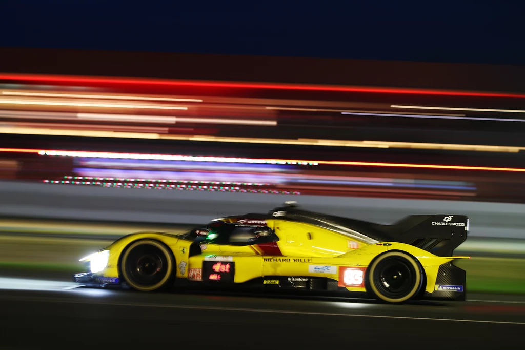 Robert Kubica na trasie Le Mans 24h Żółty samochód wyścigowy w ruchu na torze nocą, rozmycie tła podkreślające prędkość pojazdu, jaskrawe światła reflektorów i wyraźne oznaczenia zespołu wyścigowego.