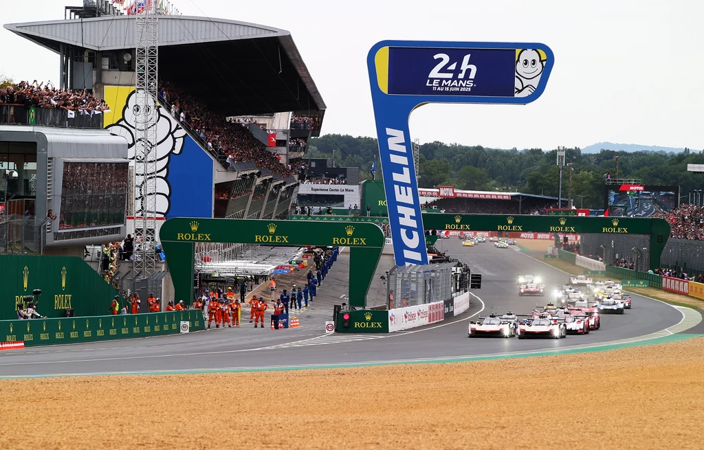 Le Mans 24 uważany jest za najtrudniejszy wyścig długodystansowy Wyścigowe samochody sportowe ruszające z linii startu podczas znanego wyścigu, tłumy kibiców na trybunach oraz sędziowie w jaskrawych kombinezonach ustawieni przy torze, widoczne banery reklamowe i oznaczenia 24h Le Mans.