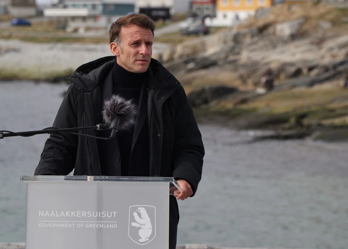 Prezydent Francji Emmanuel Macron złożył wizytę na Grenlandii Mężczyzna w eleganckim czarnym płaszczu wygłasza przemówienie na zewnątrz, stojąc za mównicą z napisem 'Government of Greenland', na tle skalistego krajobrazu i zabudowań w oddali