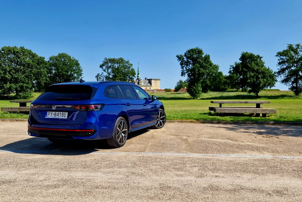 Volkswagen kusi klientów konkurencyjną ceną na hybrydy plug-in, które kosztują niewiele więcej niż auta z silnikami wysokoprężnymi Niebieskie kombi zaparkowane na żwirowym parkingu, w tle widoczne zielone drzewa i budynek przypominający pałac lub zamek, pogodny i słoneczny dzień