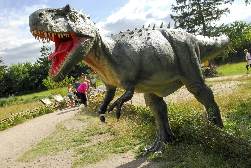 Albertozaur z Kanady także miał wyraźne rogi nad oczodołami Duży model dinozaura z otwartą paszczą, stojący na ścieżce w parku, w tle ludzie oglądający ekspozycję oraz zielone krzewy i drzewa