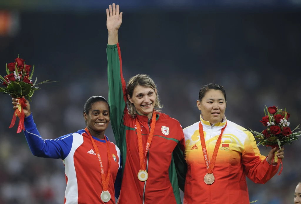Yipsi Moreno (z lewej) na podium w Pekinie. Olimpijskie złoto po dyskwalifikacji Aksany Miankowej dostała osiem lat później Trzy uśmiechnięte zawodniczki stoją na podium z medalami na szyjach i bukietami kwiatów w dłoniach, środkowa zawodniczka unosi rękę, wszyscy ubrani są w narodowe dresy reprezentacyjne.