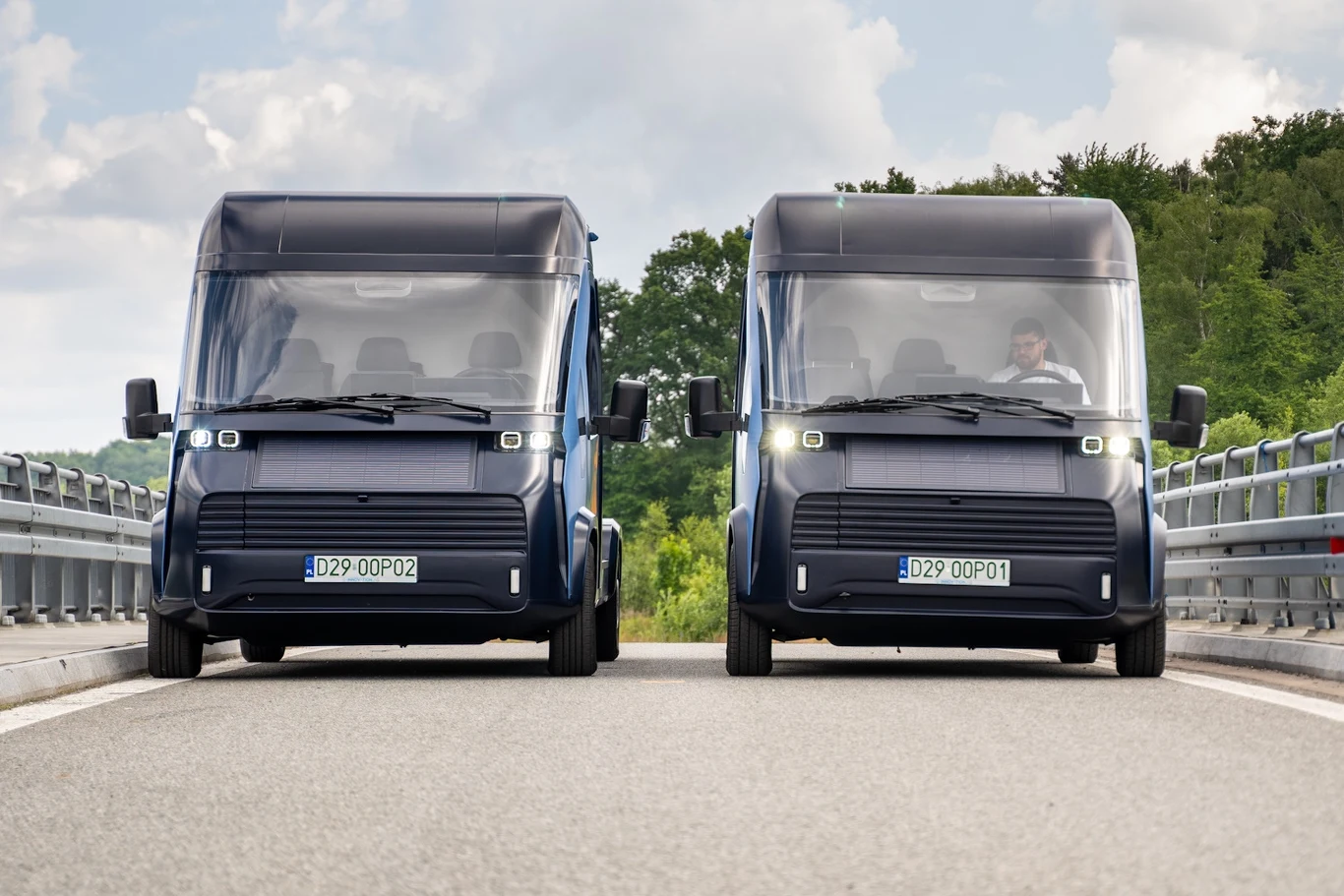 Polskie elektryczne samochody dostawcze nie będą powstawać w kraju? Ich twórcy nie zakwalifikowali się do wsparcia w ramach KPO. Przegrali z ElectroMobility Poland Dwa nowoczesne dostawcze samochody elektryczne stoją obok siebie na pustym odcinku drogi pośród zieleni, jeden prowadzony przez mężczyznę, drugi pusty.