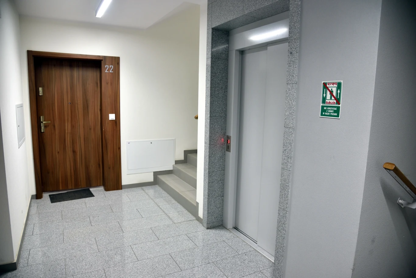 Zgodnie z przepisami, jeśli właściciel chce podnieść czynsz, musi złożyć najemcy pisemne oświadczenie o podwyższeniu stawki. Korytarz w budynku mieszkalnym z drzwiami do mieszkania oznaczonym numerem 22, windą i klatką schodową, na ścianie widoczny znak informacyjny.