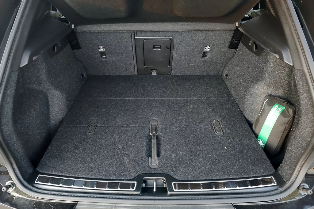 Bagażnik Volvo EX40 ma sporą pojemność i podwójną podłogę Pojemny bagażnik samochodu z wykładziną, z boczną wnęką zawierającą apteczkę oraz praktycznymi zaczepami i klapką na środku tylnego oparcia.