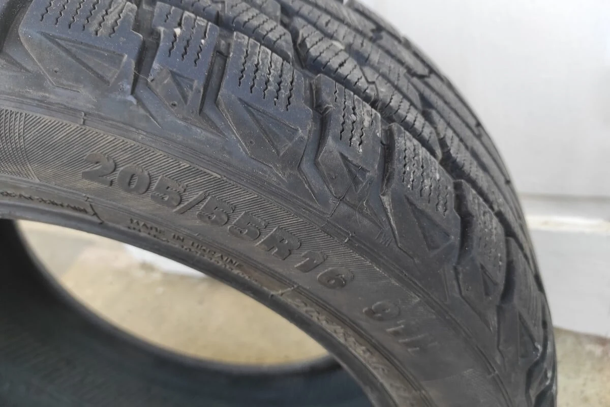 Opona samochodowa z wyraźnie widocznym bieżnikiem i oznaczeniem rozmiaru na bocznej ściance na tle jasnej powierzchni.