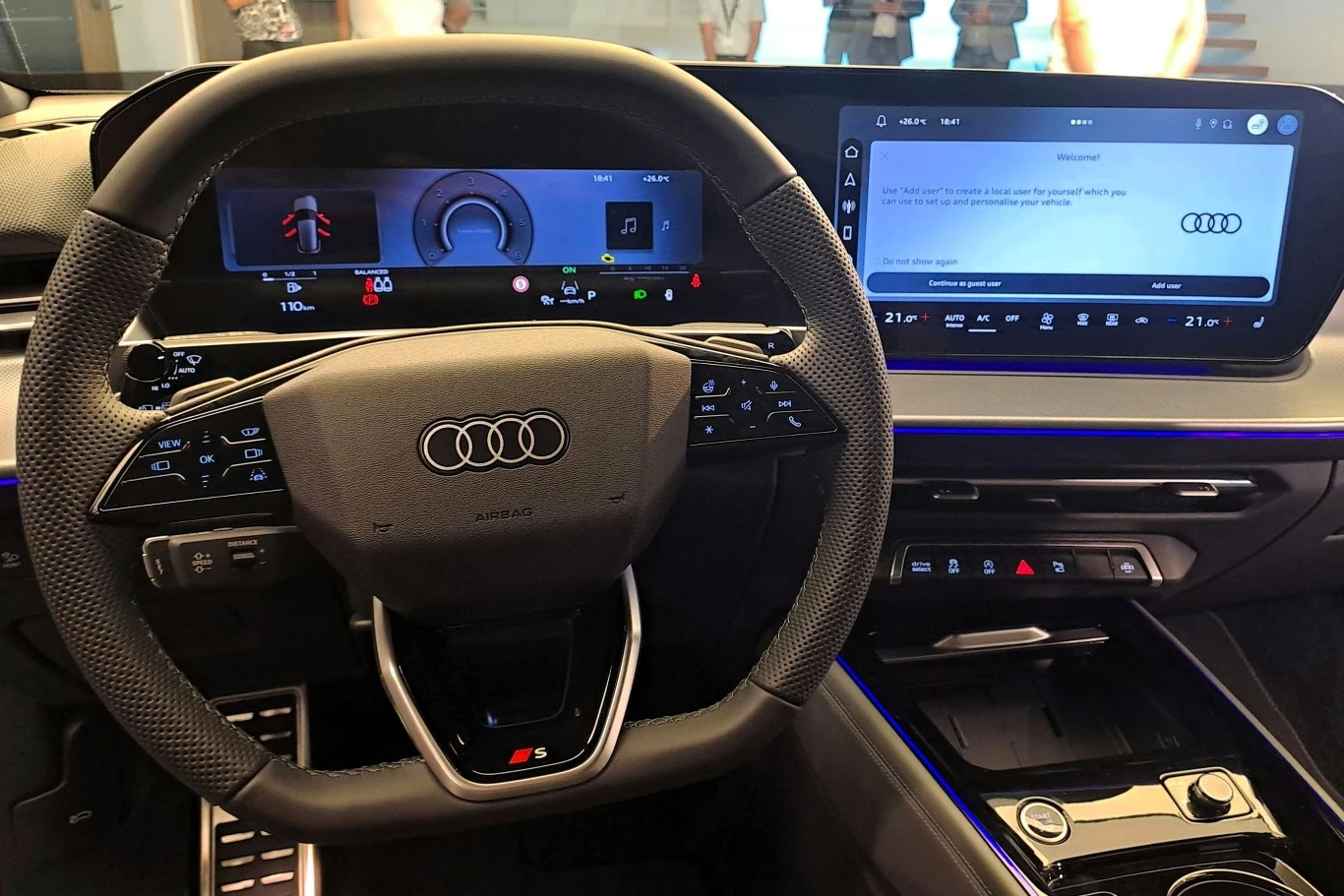 Nowoczesna deska rozdzielcza Audi z cyfrowym kokpitem, dużym ekranem dotykowym po prawej stronie oraz sportową, perforowaną kierownicą z logo S. Otoczenie utrzymane w estetyce futurystycznej, podświetlenia LED podkreślają wnętrze.