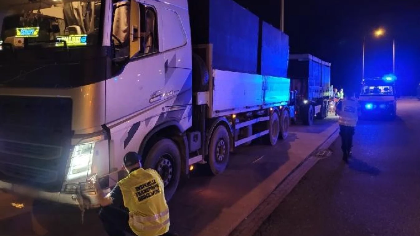 ITD przeprowadziła kontrole pojazdów. Jedno z naruszeń dotyczyło transportu wojskowego Kontrola drogowa dużej ciężarówki przez funkcjonariuszy policji na oświetlonej ulicy nocą, jeden z funkcjonariuszy kuca przy przodzie pojazdu, a w tle widoczne są policyjne radiowozy z włączonymi światłami ostrzegawczymi.