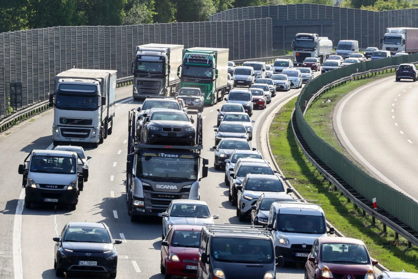Zakaz ciężarówek 1 listopada 2025 - kiedy obowiązuje, wyjątki, mandaty? Korki na autostradzie, liczne samochody osobowe i ciężarowe jadące w gęstym ruchu w obu kierunkach, po jednej stronie widoczne ekrany dźwiękochłonne i pas zieleni, po drugiej ogrodzenie ochronne.