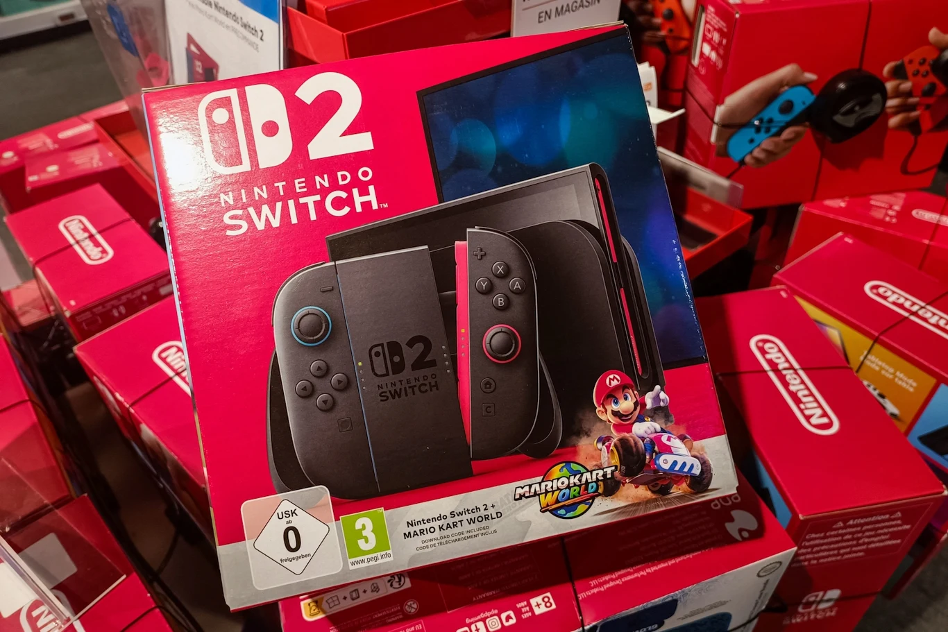 Nintendo Switch 2 Opakowanie konsoli Nintendo Switch 2 z kontrolerami Joy-Con oraz grafiką promującą grę Mario Kart World, umieszczone na tle innych podobnych pudełek z tej samej serii.