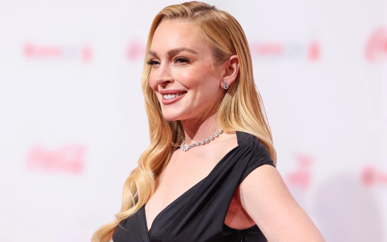 Lindsay Lohan Lindsay Lohan w długich blond włosach i ciemnej sukni pozuje przed ścianą z czerwonymi napisami