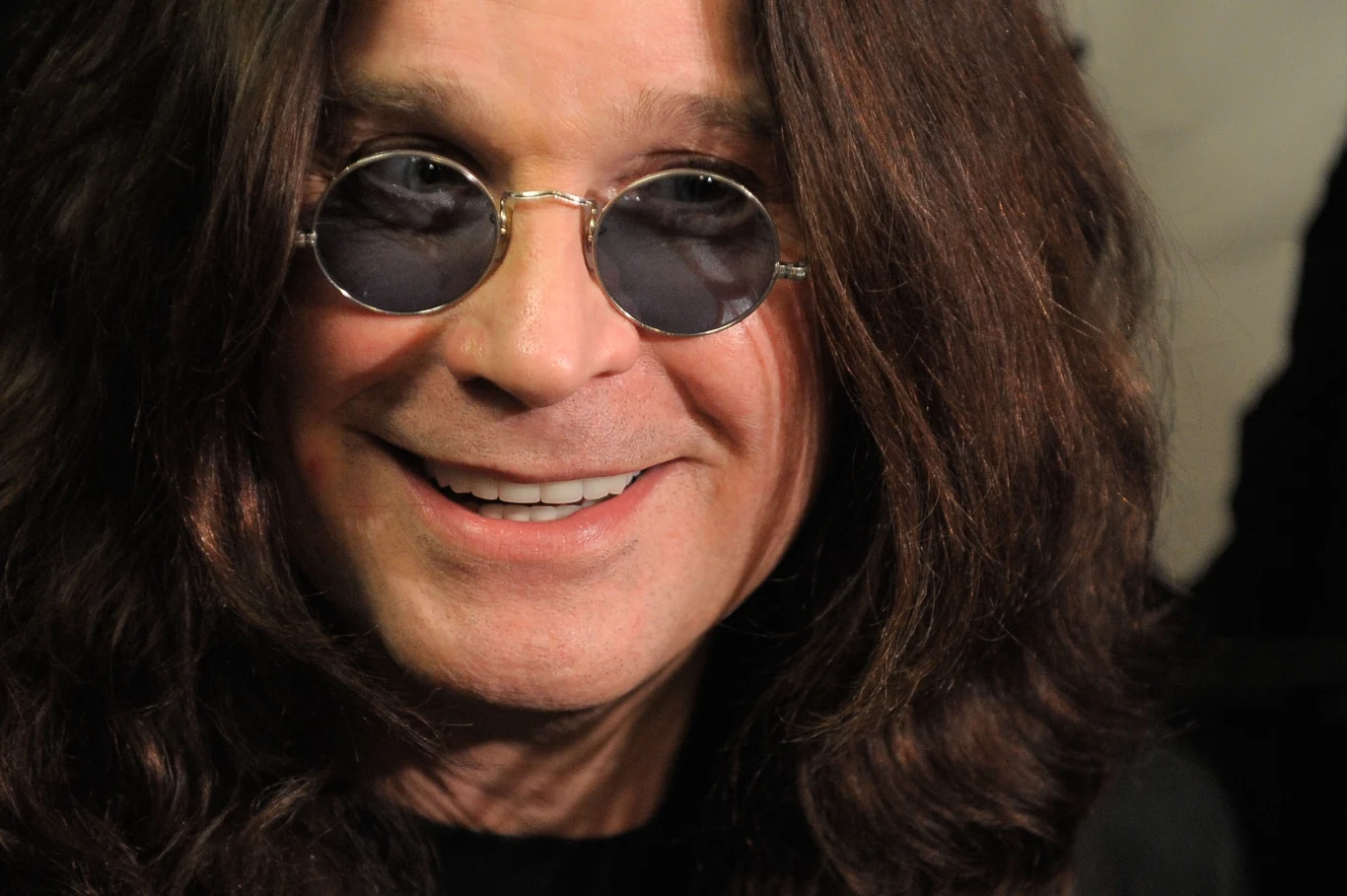 Ozzy Osbourne sprzedaje swoje DNA Uśmiechnięty mężczyzna o długich, ciemnych włosach, w okrągłych okularach przeciwsłonecznych, zbliżenie twarzy w dobrze oświetlonym otoczeniu.