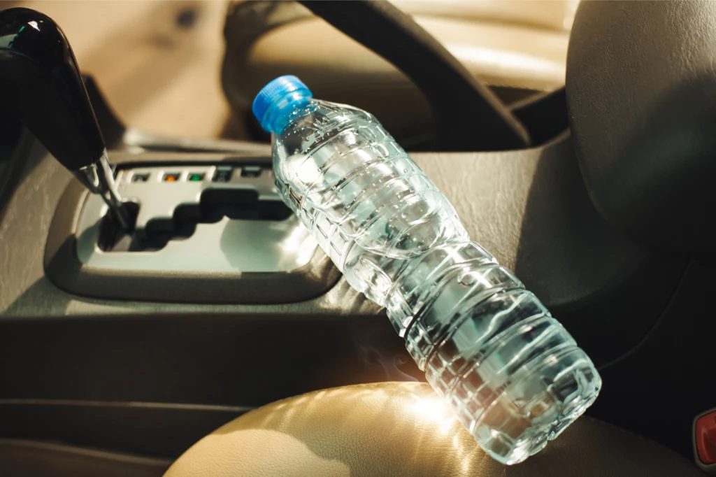 Wystarczy jeden łyk wody, aby przenieść bakterie z jamy ustnej do wnętrza butelki. Plastikowa butelka wody mineralnej leży na konsoli środkowej samochodu obok drążka automatycznej skrzyni biegów, w tle widoczne są skórzane siedzenia.