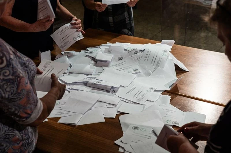 Dojdzie do ponownego przeliczenia głosów w dwóch komisjach Stół zasypany kartami do głosowania, wokół którego stoją osoby liczące głosy, przedstawione są jedynie fragmenty ciał bez rozpoznawalnych twarzy.