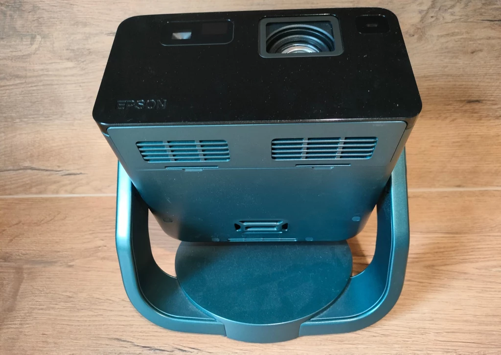 Epson EF-22 Nowoczesny projektor multimedialny marki Epson ustawiony na stojaku, widok z góry, na tle drewnianej powierzchni.