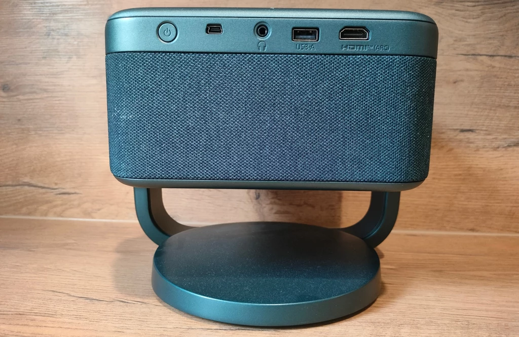 Epson EF-22 Projektor multimedialny umieszczony na okrągłej podstawie, z widocznym panelem złącz i portów oraz tekstylną osłoną głośników, całość na tle drewnianej powierzchni.