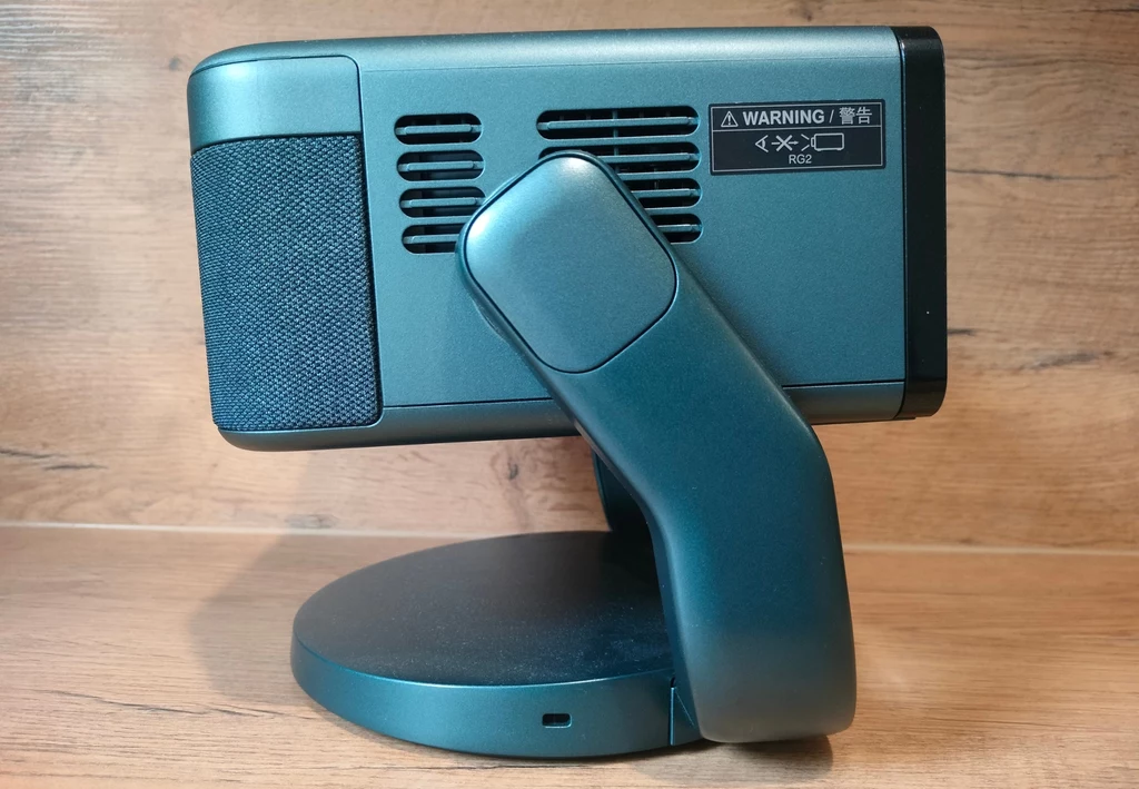 Epson EF-22 Projektor biurowy na stabilnej, ruchomej podstawie, w tle drewniana powierzchnia, na urządzeniu widoczne kratki wentylacyjne i naklejka ostrzegawcza.