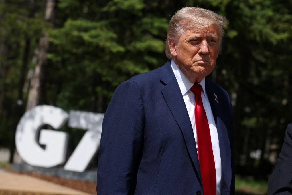 Donald Trump miał zatwierdzić plany ataku na Iran Mężczyzna w ciemnym garniturze i czerwonym krawacie stoi na tle dużych białych liter G7 ustawionych w otoczeniu zielonych drzew.