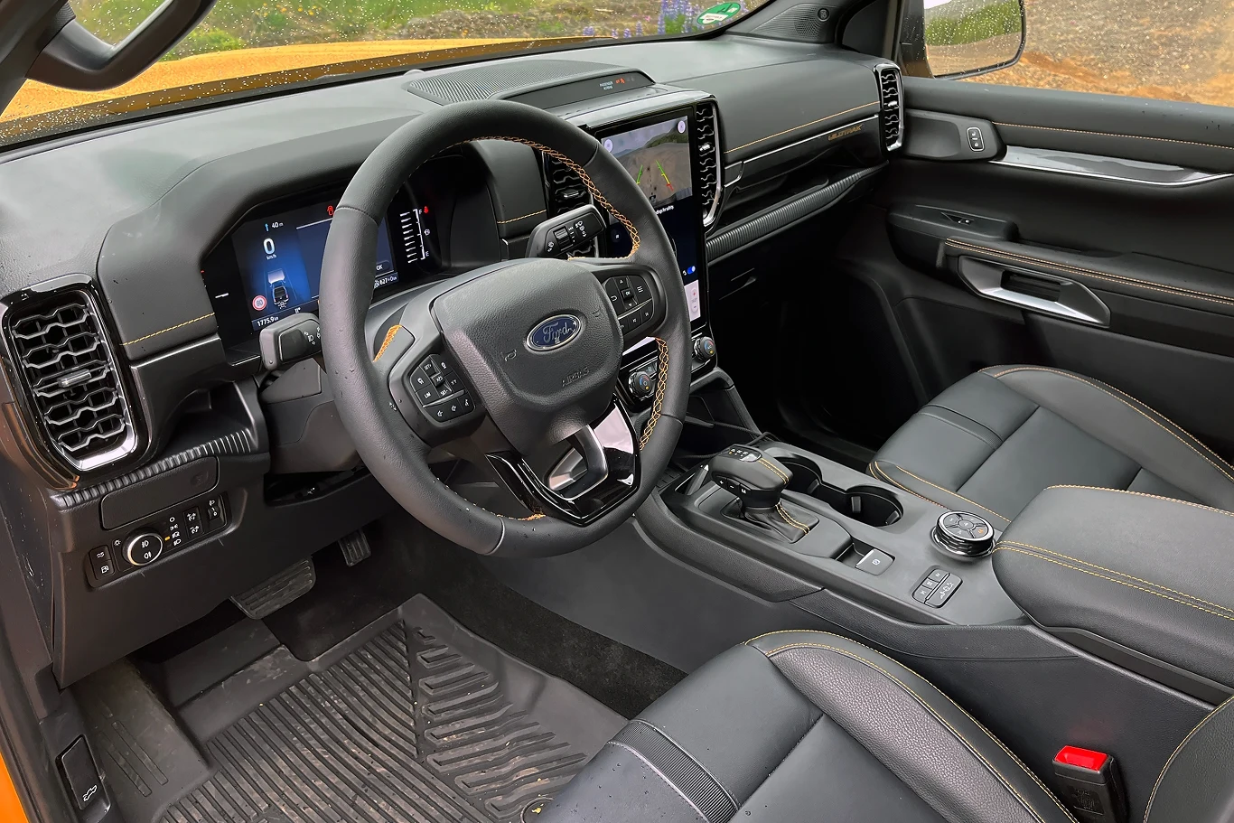 Nowoczesne wnętrze samochodu Ford z widocznymi przednimi fotelami, kierownicą, elektroniczną deską rozdzielczą oraz dużym ekranem dotykowym na konsoli centralnej, wykończone czarną skórą z żółtymi przeszyciami.
