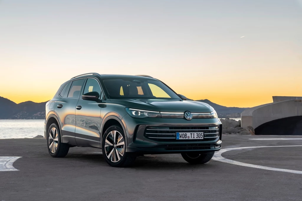 Nowy Tiguan nie tyle próbuje być modny, co wyznacza zupełnie nowy kierunek Zielony SUV marki Volkswagen zaparkowany na otwartym terenie przy zachodzie słońca, w tle góry i fragment mostu.