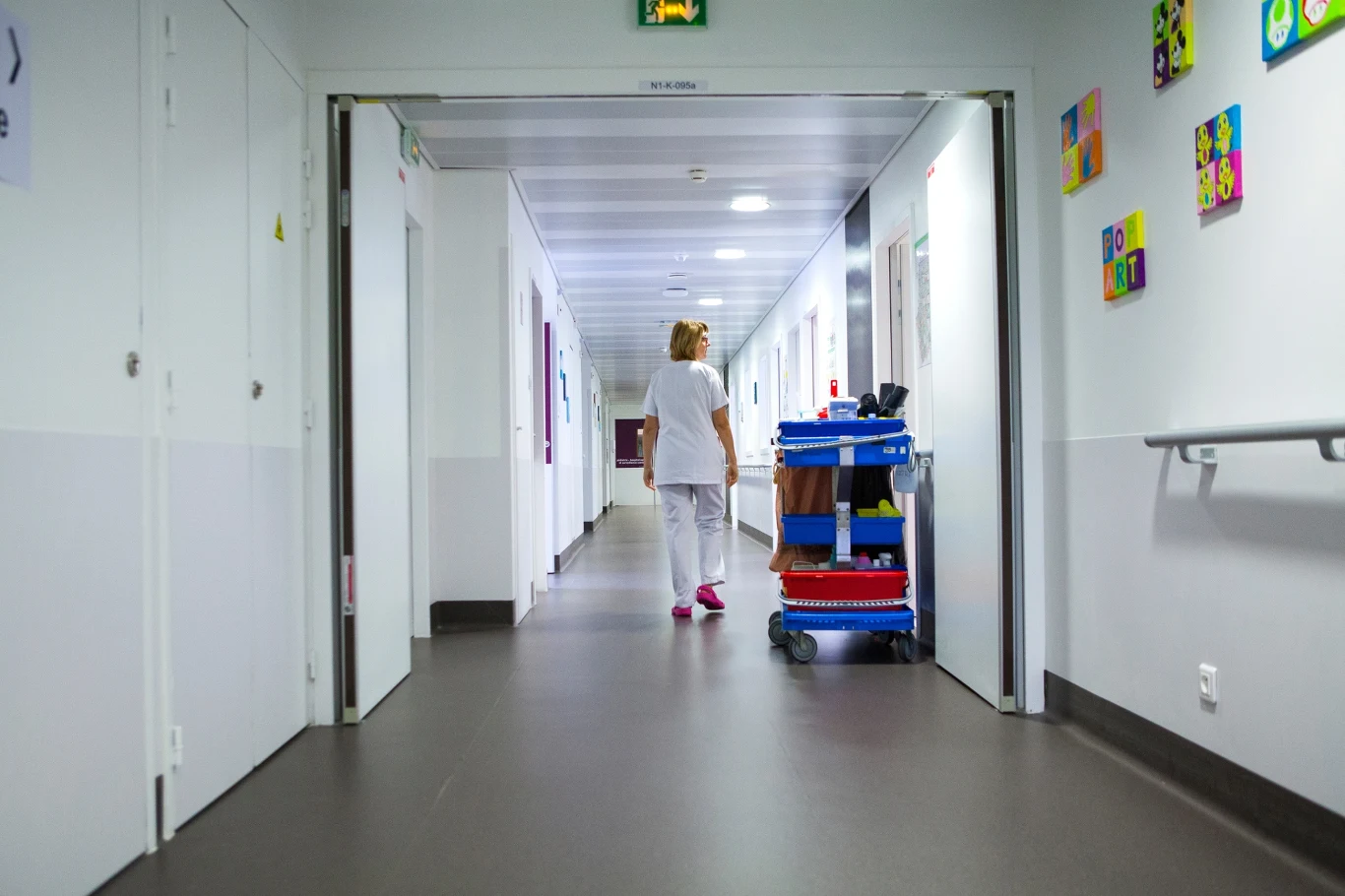 We Francji kilkoro dzieci trafiło do szpitala z objawami zatrucia Korytarz szpitalny z pracownicą w białym uniformie pchającą wózek do sprzątania, ściany ozdobione kolorowymi obrazkami, jasne oświetlenie, atmosfera porządku i czystości.