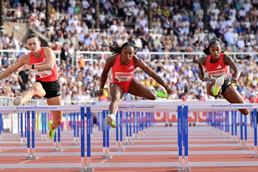 Nadine Visser, Grace Stark i Ackera Nugent Trzy zawodniczki podczas biegu przez płotki na stadionie, w trakcie dynamicznego przeskakiwania przez przeszkody, trybuny wypełnione liczną publiką w tle, wszyscy skupieni na sportowej rywalizacji.