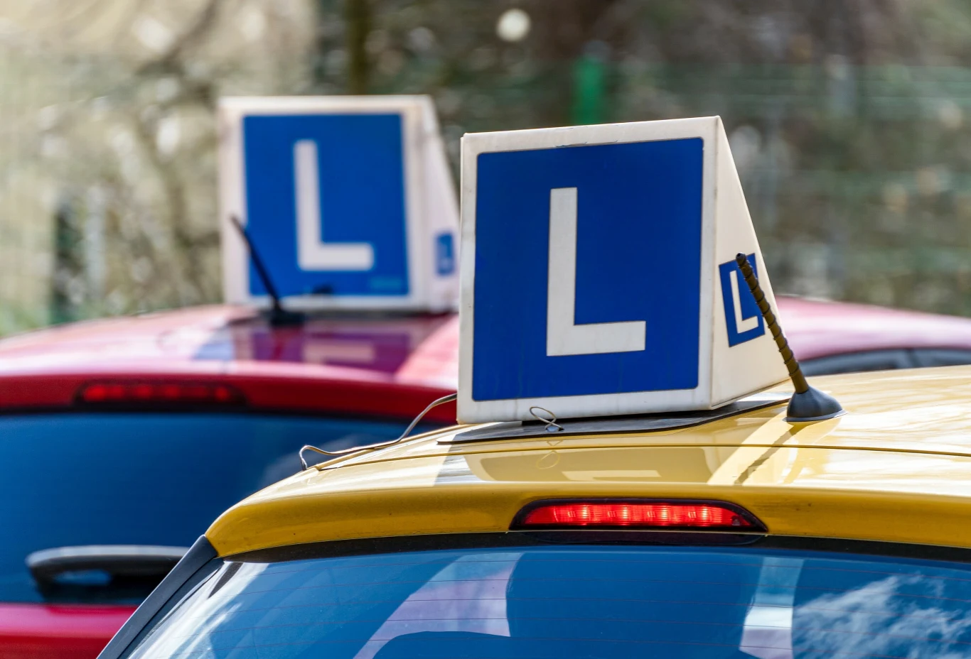 1 lipca wchodzą w życie kontrowersyjne zmiany w egzaminie na prawo jazdy Samochody nauki jazdy z oznaczeniem litery L na dachu, kolorowe pojazdy ustawione blisko siebie, skupienie na znakach identyfikujących auta do szkolenia kierowców.