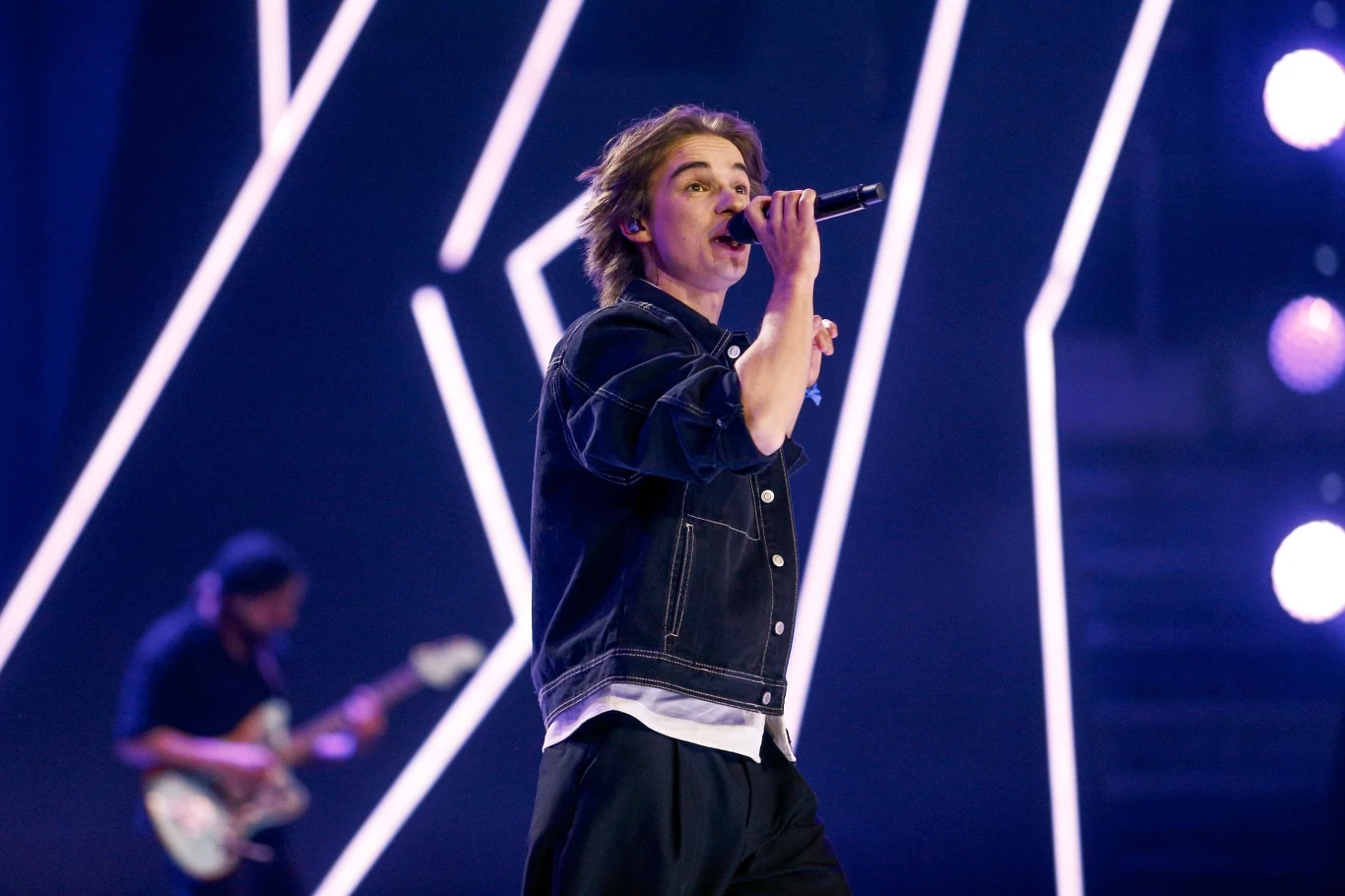 Wiktor Waligóra był jedną z gwiazd Wodecki Twist Młody mężczyzna śpiewający do mikrofonu na scenie koncertowej z jasnym oświetleniem, w tle gitarzysta i nowoczesna aranżacja świateł LED.