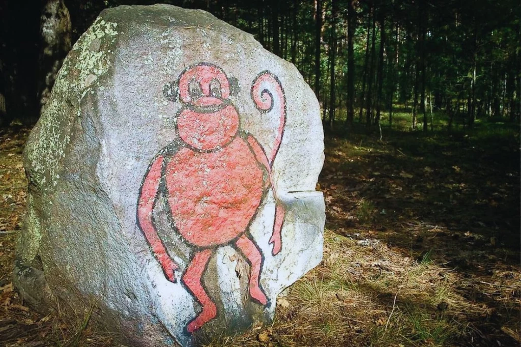 Głaz z Czerwoną Małpą i związane z nim legendy mogą spowodować ciarki na ciele Duży głaz stojący w lesie, na którym widnieje rysunek stylizowanej czerwonej małpy z zakręconym ogonem.