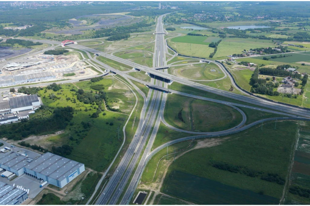 Trzypoziomowy węzeł Gliwice-Sośnica ma 16 wiaduktów i 36 zjazdów. Zdjęcie zostało wykonane w 2013 r. Rozbudowany węzeł autostradowy pośród zielonych terenów, liczne zjazdy i wiadukty otoczone obszarem przemysłowym i polami, w tle widoczne mniejsze zabudowania i lasy.