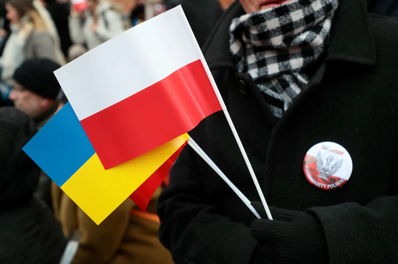 Flagi Polski i Ukrainy; zdj. ilustracyjne Dwie flagi, polska i ukraińska, trzymane razem przez osobę ubraną w czarny płaszcz i szalik w kratę, z przypinką na klapie płaszcza.