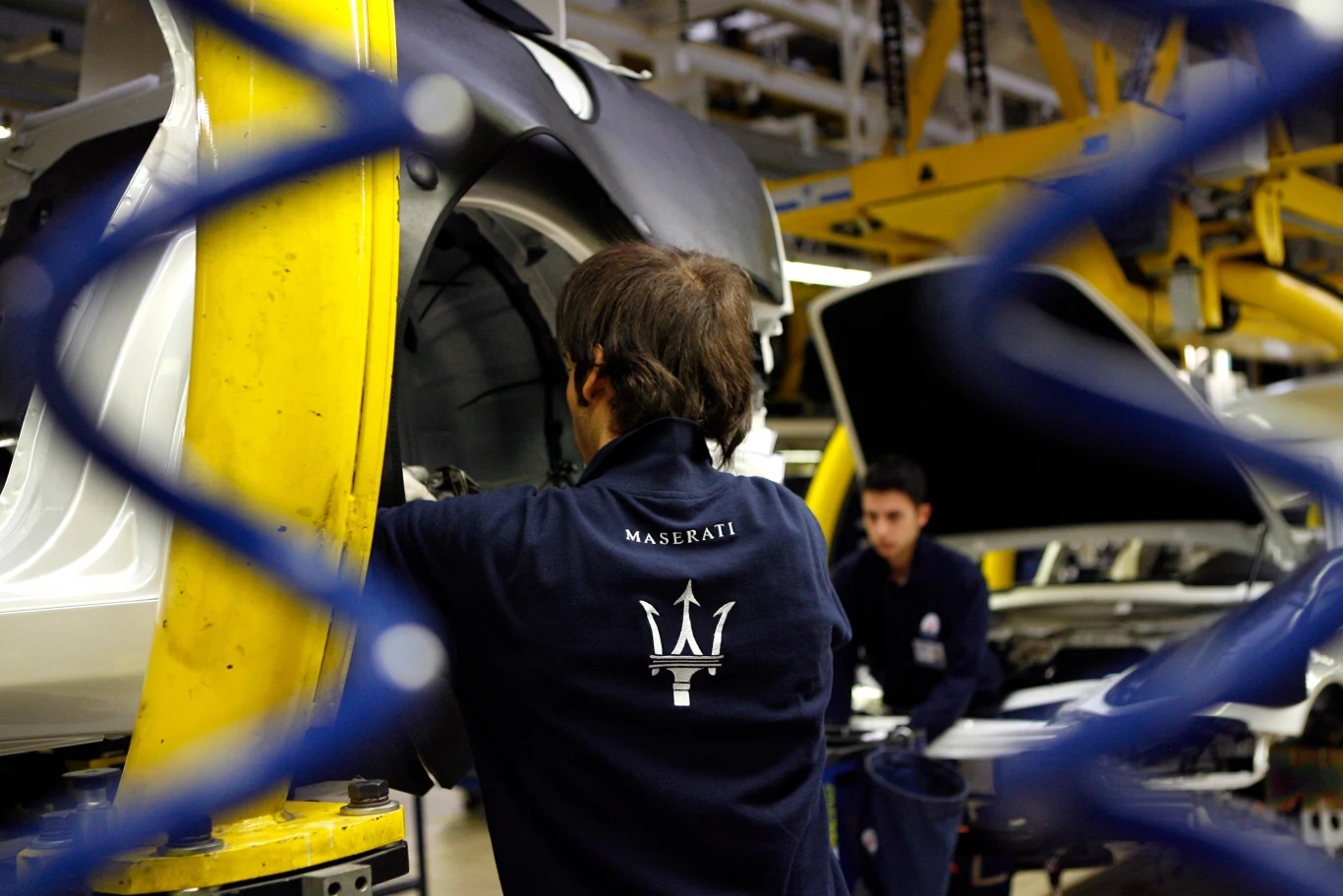 Stellantis planuje restrukturyzację swojego imponującego portfolio. Pracownicy linii produkcyjnej w fabryce Maserati zajmują się składaniem karoserii auta w nowoczesnym, dobrze oświetlonym zakładzie przemysłowym.
