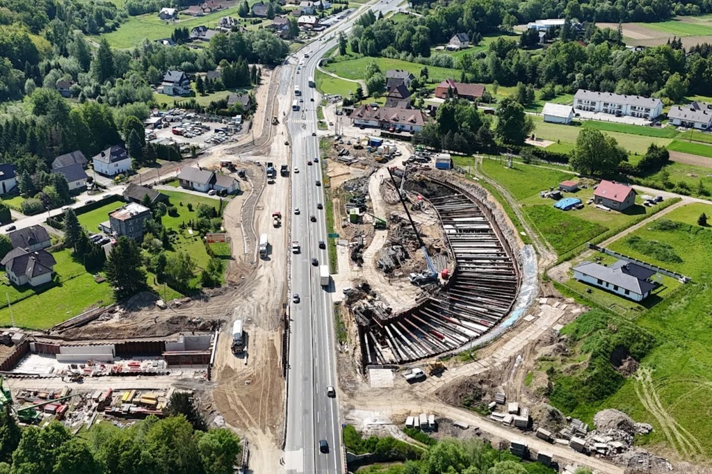 Tunel pod zakopianką budowany jest metodą klasyczną. Mimo wszystko jest to wyzwanie Rozległy plac budowy przy głównej drodze z nowo powstającym wiaduktem, otoczony samochodami i maszynami budowlanymi, w tle zielone tereny i zabudowa jednorodzinna.