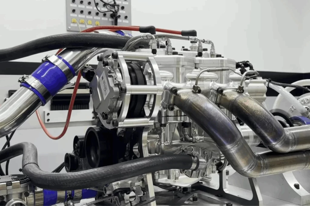 Za sprawą niewielkich rozmiarów i dużej mocy silnik Rev Force idealnie sprawdziłby się w motocyklach. Kompleksowy układ silnika z widocznymi metalowymi przewodami, silnikiem elektrycznym i elementami montażowymi, sfotografowany w sterylnym, technicznym otoczeniu laboratoryjnym.