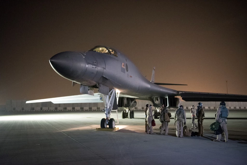 Bombowiec B-1B Lancer z 34 Eskadrze Bombowej w bazie Al Udeid w 2018 roku Wojskowy samolot na płycie lotniska po zmroku, grupa żołnierzy w mundurach przygotowuje się do wejścia na pokład