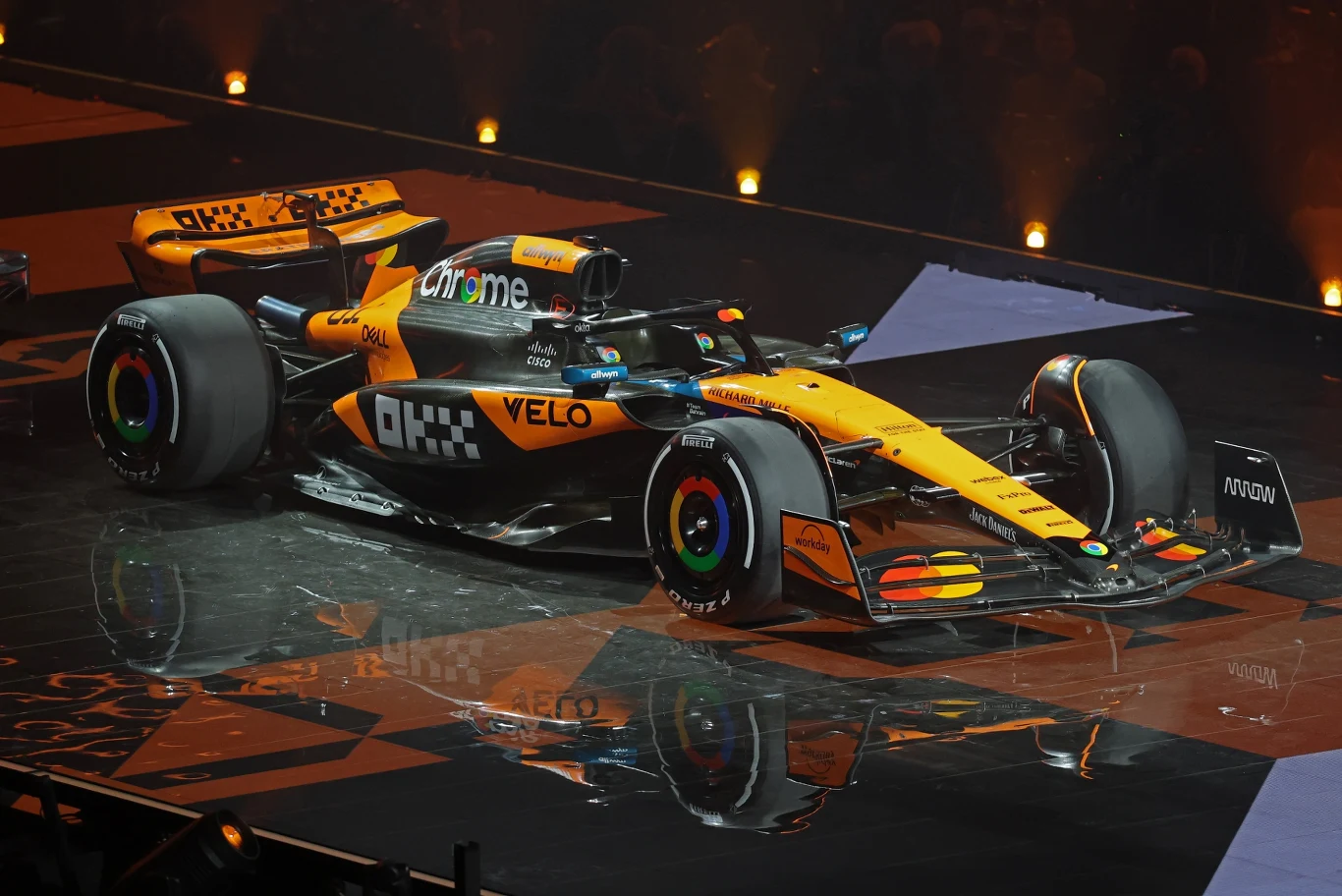 McLaren Samochód wyścigowy Formuły 1 w żółto-czarnych barwach z widocznymi logotypami sponsorów prezentowany na oświetlonej scenie.