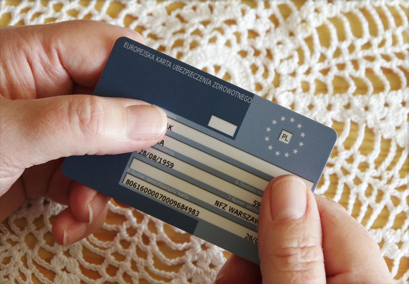 EKUZ wydawana bezpłatnie. Europejska Karta Ubezpieczenia Zdrowotnego trzymana w dłoniach osoby, na tle białej serwetki.