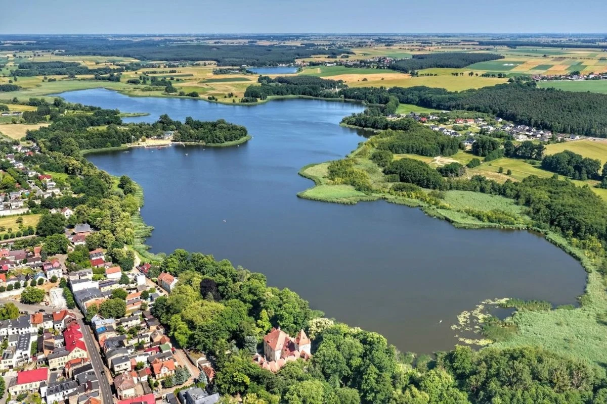 Lubuskie to nie tylko kraina jezior. Sprawdź, co warto zobaczyć/ FOT. Grzegorz Walkowski Jezioro otoczone zielenią i polami uprawnymi, w dolnej części kadru widoczna część miasta z zabytkowym kościołem ukrytym wśród drzew, w oddali rozległe pola i lasy.