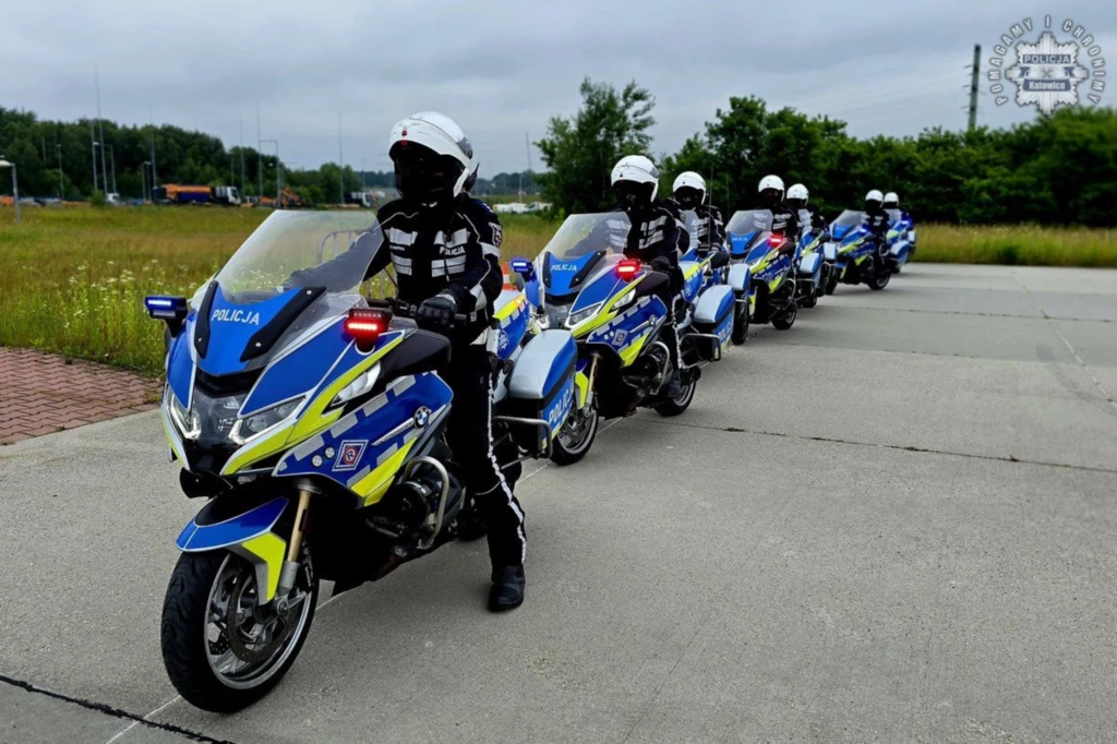 W 2023 r. Polska Policja zakupiła 478 egzemplarzy motocykli BMW R 1250 RT. Grupa policyjnych motocyklistów ubranych w czarne mundury i białe kaski siedzi na niebiesko-żółtych motocyklach ustawionych w szeregu na utwardzonym placu, w tle widoczne zielone drzewa i trawa.