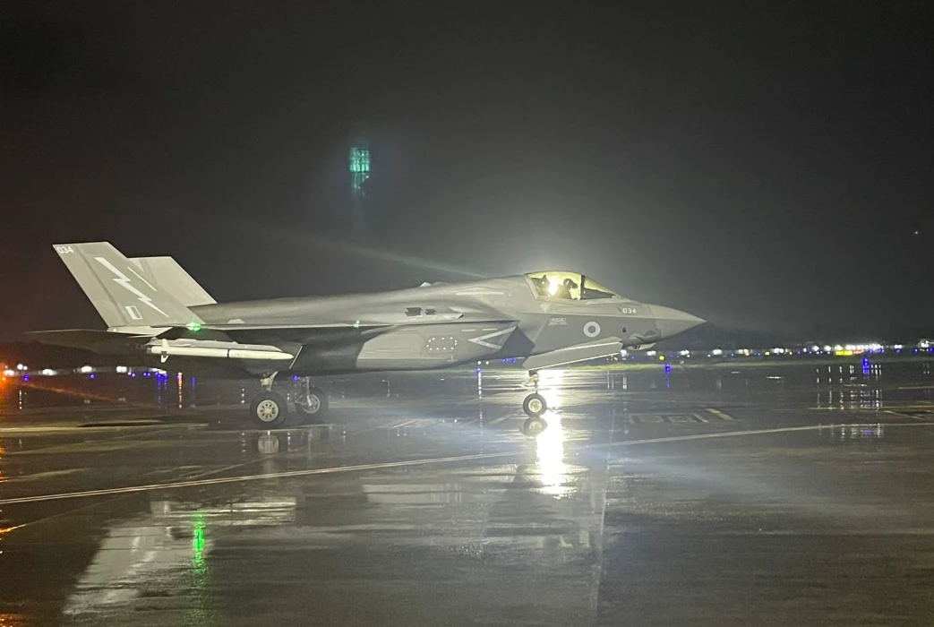 Indie. Brytyjski F-35B od 10 dni stoi w deszczu i czeka na naprawę Nowoczesny myśliwiec wojskowy F-35 stoi na oświetlonym, mokrym pasie startowym nocą, światła odbijają się od mokrej powierzchni, w kabinie siedzi pilot.
