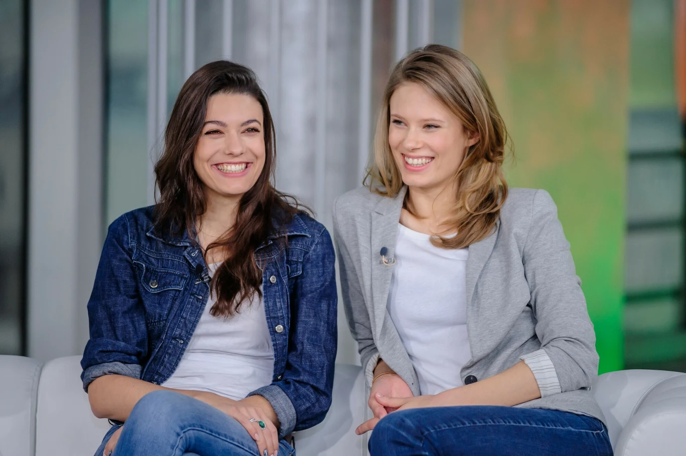 Natalia Pietrucha i Julia Pietrucha w 2016 r. Dwie młode kobiety siedzące na kanapie, ubrane swobodnie, obie z uśmiechem, w jasnym, nowoczesnym wnętrzu.