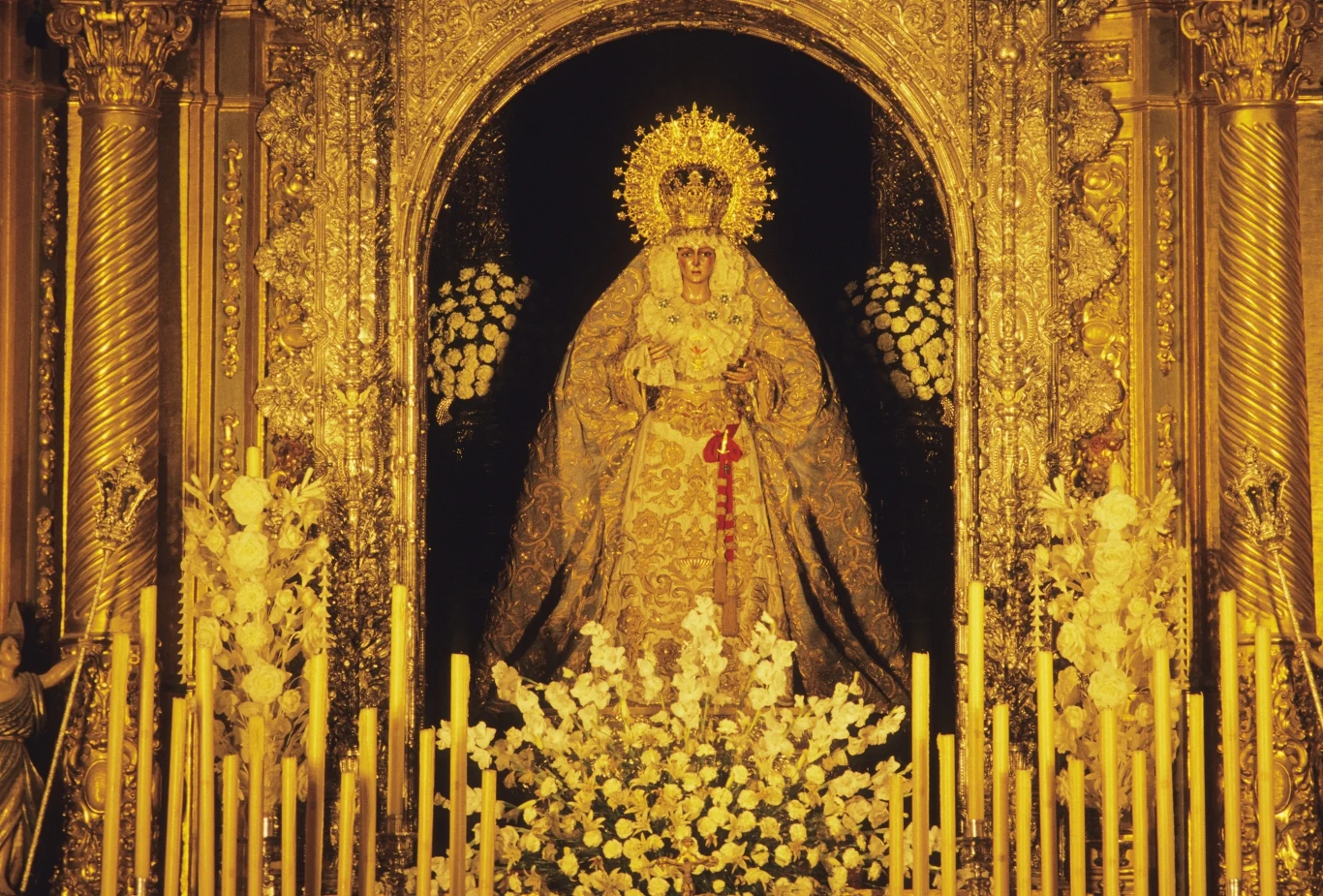 Figura Matki Boskiej z Macareny przeszła renowację Bogato zdobiona figura Matki Boskiej z koroną i aureolą w otoczeniu licznych świec, białych kwiatów i złotych dekoracji umieszczona w ołtarzu.