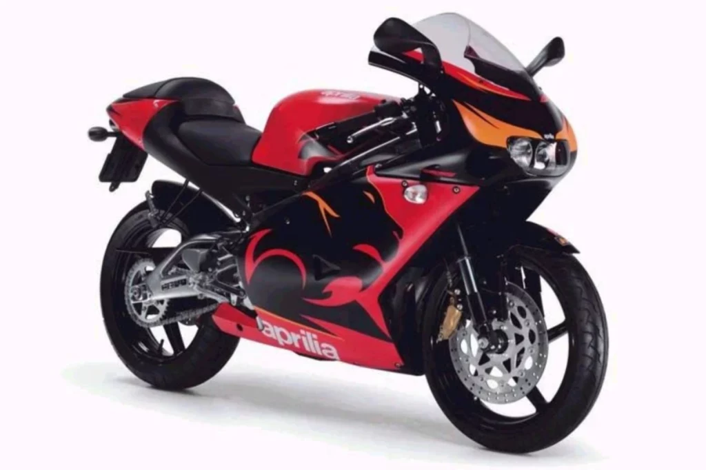 Aprilia RS 125 znacznie dłużej, bo aż do 2006 roku sprzedawana była z dwusuwową jednostką. Sportowy motocykl w czerwono-czarnych barwach z widocznym logo marki aprilila, ozdobiony graficznym motywem płomieni i pantery, ustawiony na białym tle.